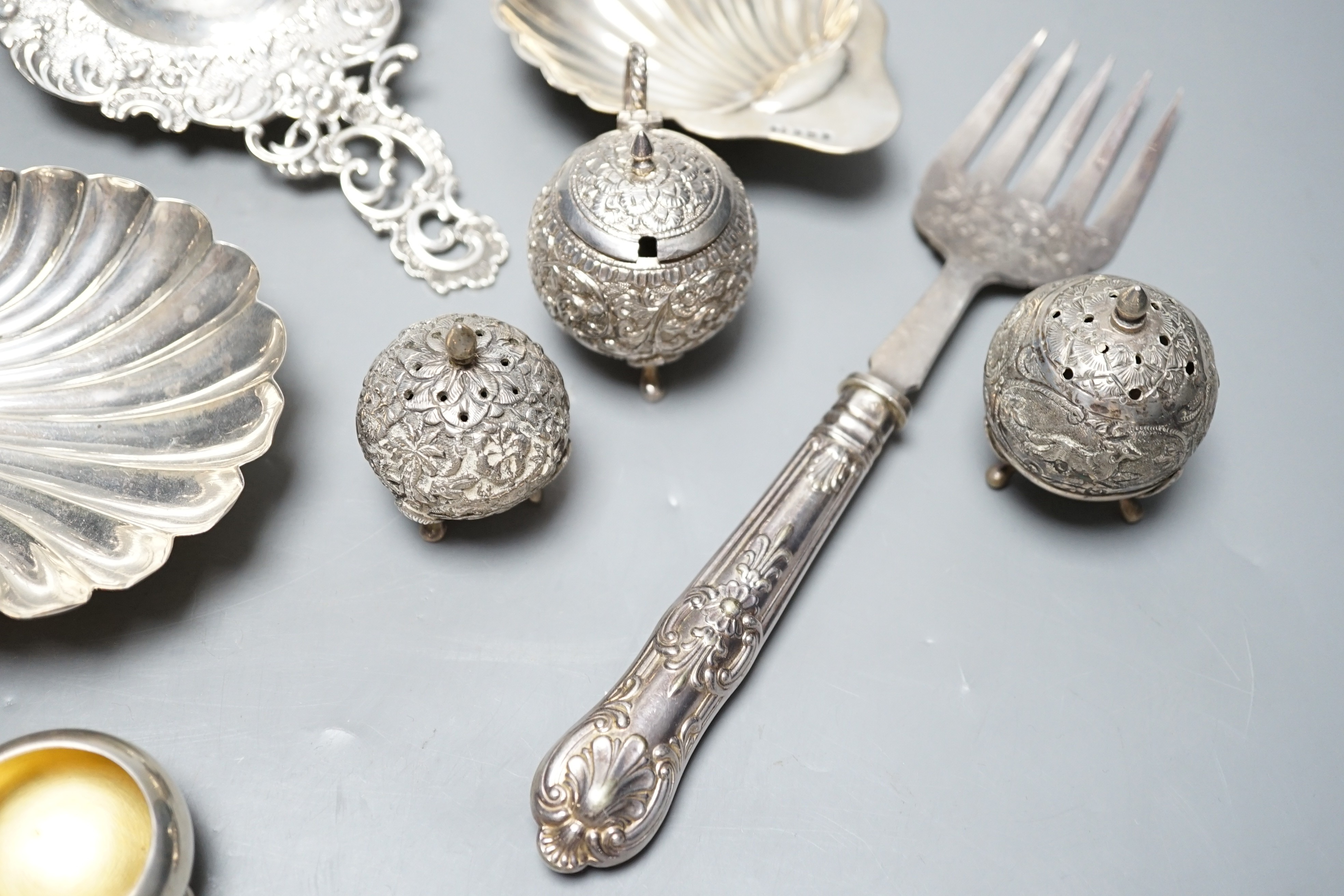 Small silver including two butter shells, a continental silver tea strainer, English tea strainer, pair of salts, swizzle stick, serving fork, two pepperettes and an Indian white metal three piece condiment set.
